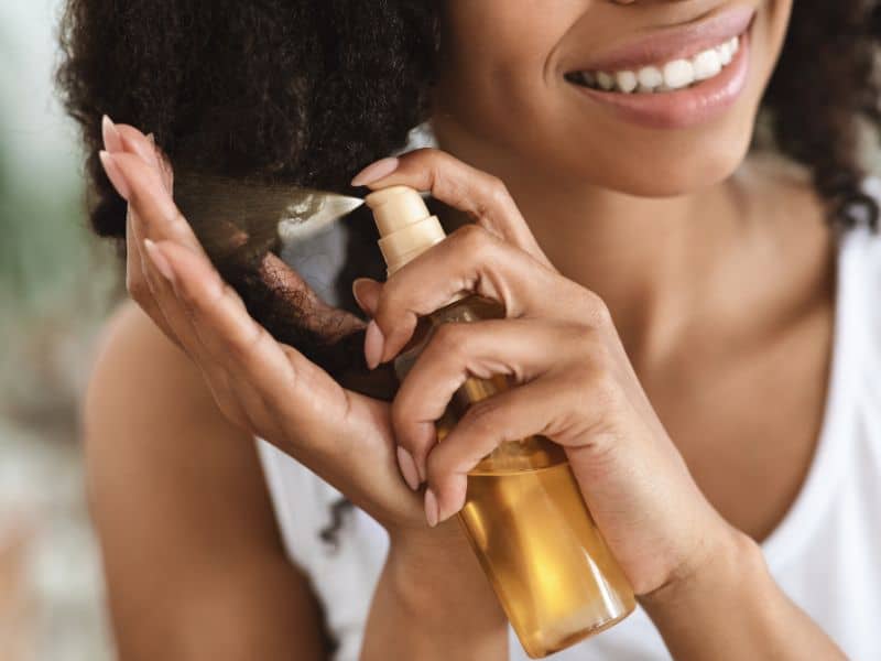 How to Make Hair Color Last Longer - woman spraying hair oil into her natural hair